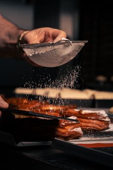 Chef carefully sprinkles powdered sugar over pastries in a professional kitchen. Perfect for culinary themes.