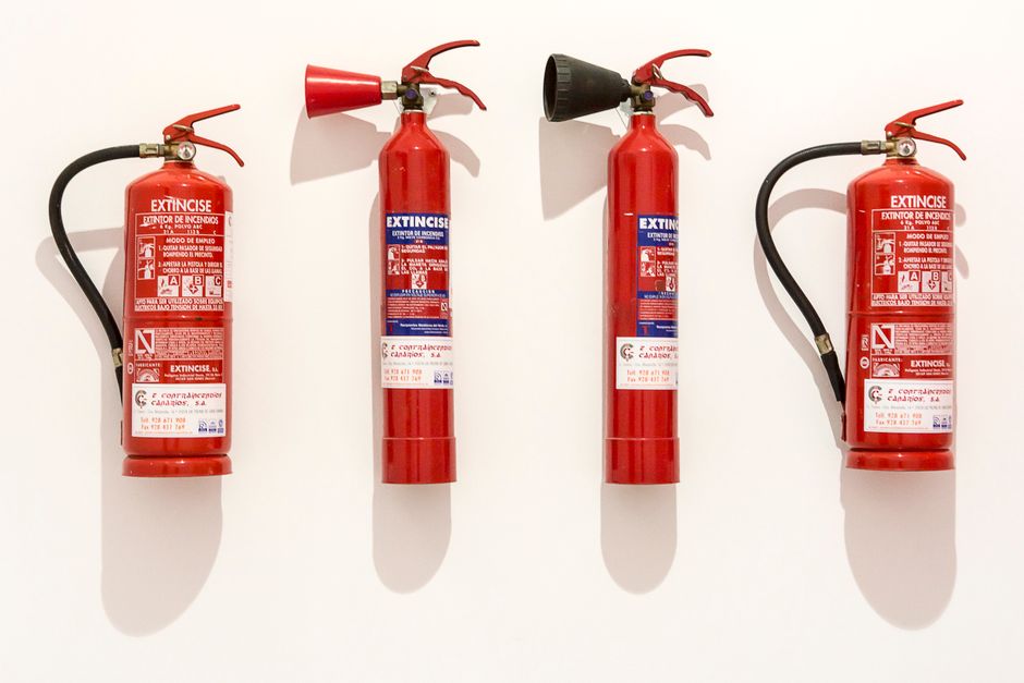 Four red fire extinguishers hanging on a clean white wall in an orderly fashion.