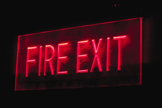 Brightly lit red neon fire exit sign illuminating in a dark setting.